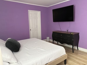 A bedroom with a bed, a dresser, a television, and a door. - Colorful 3 BDRM home w/ pool (Henderson)