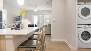 A modern kitchen with a central island, wooden chairs, a dining area, and a laundry area with Samsung washing machines. - Landing | Amazing 2BD in Loughman (Davenport)