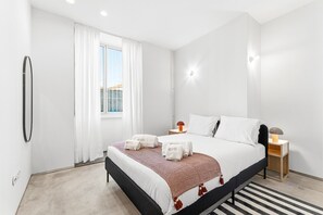Een moderne hotelkamer met een groot bed, een nachtkastje met een lamp, een raam met gordijnen en uitzicht naar buiten.