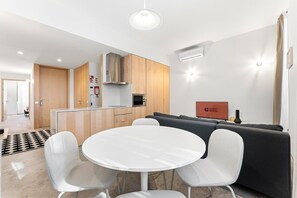 Ein modernes Wohnzimmer mit einem runden weißen Tisch, zwei Stühlen, einem grauen Sofa und einem Flachbildfernseher.