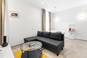 A modern living room with a sectional sofa, a glass coffee table, a white dining table, and a kitchen area with a microwave. - GuestReady- Rou 27- B (Porto)