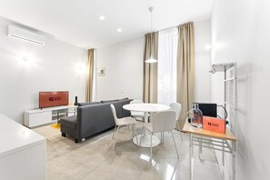 Een moderne hotelkamer met een bank, een eettafel en een televisie waarop 'GUEST READY' staat.