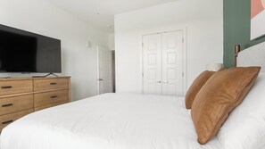 A bedroom with a bed, a TV on a wooden dresser, and a white door. - Landing | Beautiful 1BD, Clubhouse, Pool (Sarasota)