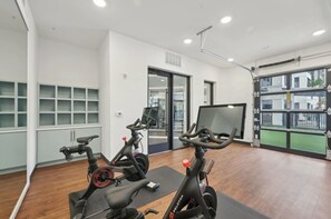 A gym with stationary bikes, a large screen, and a view of the outside. - Landing | Beautiful 1BD, Clubhouse, Pool (Sarasota)