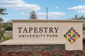 A sign for Tapestry University Park with a stone base and a colorful logo. - Landing | Incredible 1BD, Pool, Clubhouse (Sarasota)