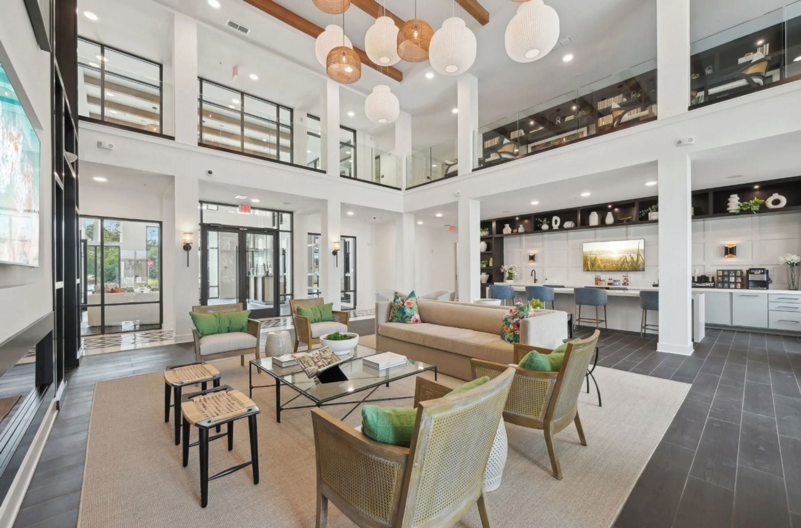 A spacious lobby with a high ceiling, a central seating area with sofas and chairs, a kitchen area with bar stools, and a staircase leading to an upper level.