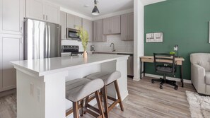 A modern kitchen with white cabinetry, a stainless steel refrigerator, a built-in oven, and a large island with bar stools. - Landing | Amazing 1BD, Pool, Clubhouse (Sarasota)