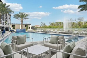 A pool area with lounge chairs and a small table, surrounded by palm trees and a building. - Landing | Amazing 1BD, Pool, Clubhouse (Sarasota)