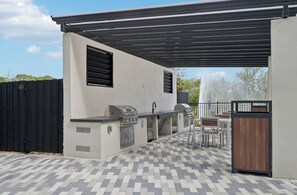 An outdoor patio with a grill, seating, and a covered area. - Landing | Modern 1BD, Gym, Pool (Sarasota)