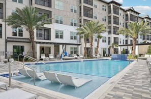 A swimming pool with lounge chairs and palm trees, surrounded by a multi-story building with balconies. - Landing | Stylish 1BD, Pool, Gym (Sarasota)