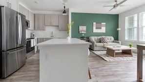 A modern kitchen with a central island, stainless steel appliances, and a green accent wall. - Landing | Stylish 1BD, Pool, Gym (Sarasota)