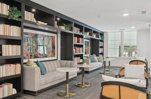 Et moderne bibliotek med bogreoler, en sofa, runde borde og et stort vindue.