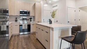 A modern kitchen with stainless steel appliances, wooden cabinets, and a central island with seating. - Landing | Incredible 2BD in North Kissimmee (Kissimmee)