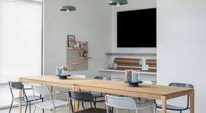 A modern meeting room with a long wooden table, six chairs, a mounted television, and wall-mounted shelves with office supplies. - Landing | Amazing 2BD in North Kissimmee (Kissimmee)