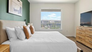 A bedroom with a bed, a dresser, a TV, and a window with a view of buildings. - Landing | Amazing 2BD in North Kissimmee (Kissimmee)