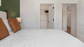 A bedroom with a bed, pillows, a nightstand, and a lamp. There are doors leading to other rooms. - Landing | Amazing 2BD in North Kissimmee (Kissimmee)
