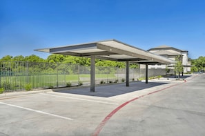 Área de estacionamento coberta com cerca de metal, piso de concreto e céu azul.
