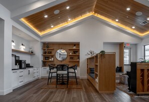 A modern kitchen with white cabinetry, wooden shelves, and a dining area with a round mirror and two chairs. - Blueground | Scofield Farms, pool, nr Walnut Creek Park (Austin)