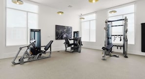 Ein Fitnessstudio mit unterschiedlichen Trainingsgeräten, großen Fenstern und einem Gemälde an der Wand.