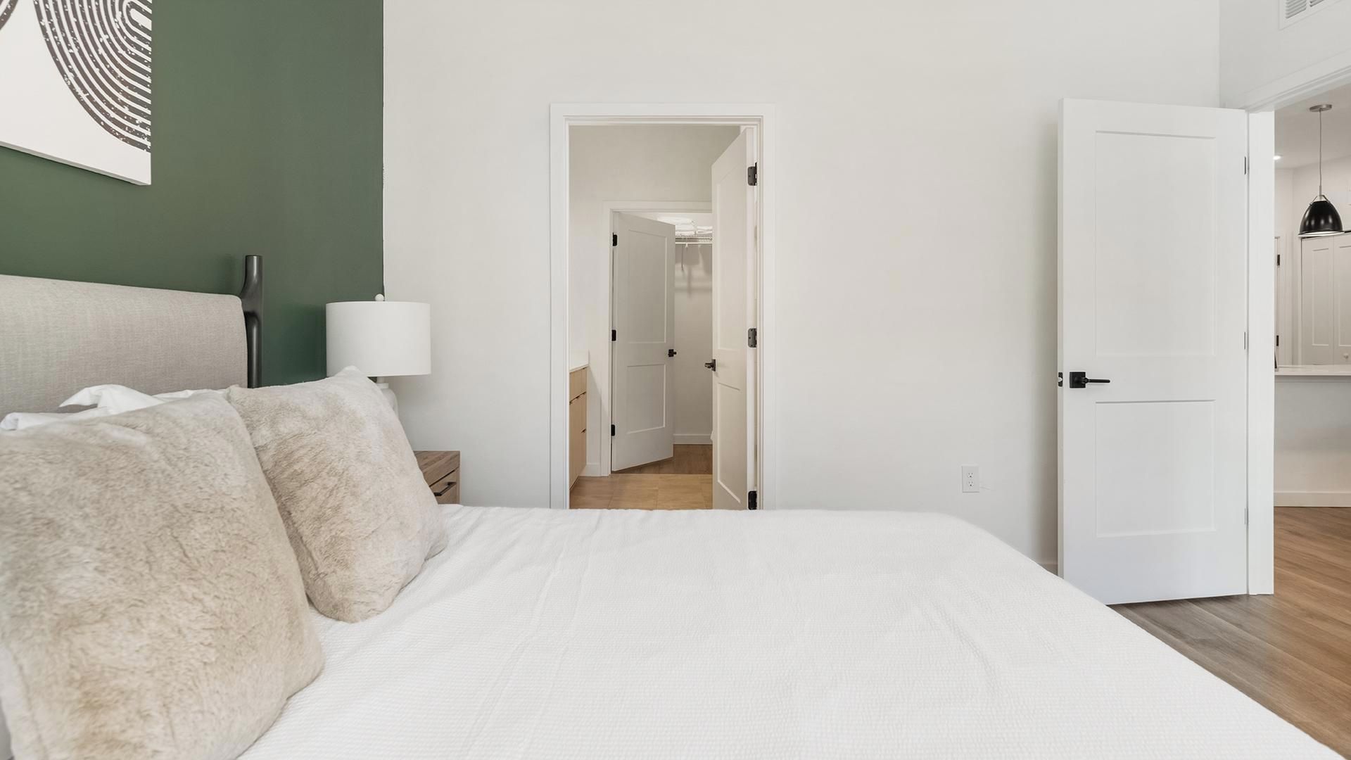 A bedroom with a large bed, a bedside lamp, and a view into an adjacent room.