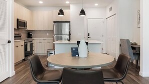 A modern kitchen with a round dining table, two chairs, and pendant lighting. - Landing | Spectacular 2BD in North Kissimmee (Kissimmee)