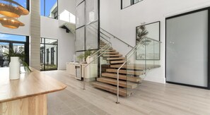 Un interior moderno con una escalera, un comedor y vistas a través de puertas de cristal.