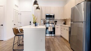 Une cuisine moderne dotée d’un îlot central, d’appareils électroménagers en acier inoxydable et de meubles de rangement en bois clair.