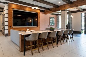 A modern kitchen with a large island, bar stools, and a built-in TV. - Landing | Incredible 2BD, Courtyard (Garland)