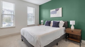 A bedroom with a bed, two bedside tables, a green accent wall, and a window with blinds. - Landing | Incredible 2BD, Courtyard (Garland)