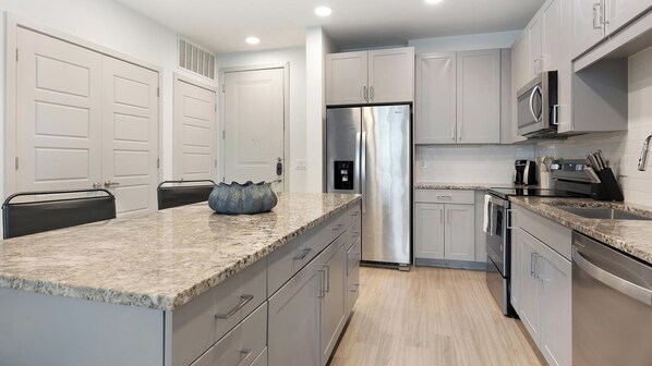 A modern kitchen with stainless steel appliances, marble countertops, and grey cabinetry. - Landing | Incredible 2BD, Courtyard (Garland)