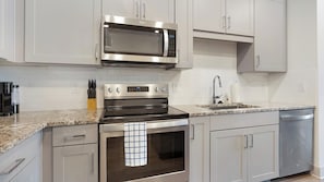 A modern kitchen with stainless steel appliances, white cabinetry, and a granite countertop. - Landing | Chic 2BD, Courtyard (Garland)