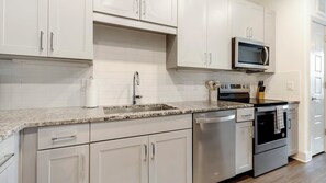 A modern kitchen with white cabinets, a granite countertop, stainless steel appliances, and a microwave. - Landing | Spectacular 1BD, Courtyard (Garland)