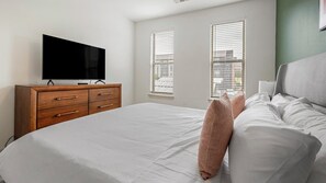 A bedroom with a bed, a wooden dresser, a television, and two windows with blinds. - Landing | Spectacular 1BD, Courtyard (Garland)