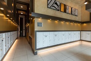 A hallway with lockers, a sign indicating the mall room, and artwork on the walls. - Landing | Spectacular 1BD, Courtyard (Garland)