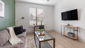 Ein modernes Wohnzimmer mit einer Couch, einem Couchtisch, einem Fernseher und einem Schreibtisch mit einem Stuhl.