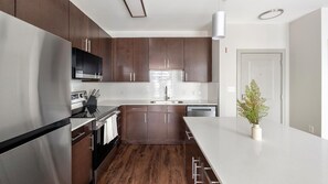 A modern kitchen with dark wood cabinets, stainless steel appliances, and a white countertop. - Landing | Beautiful 1BD, Gym (Birmingham)