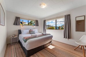 Une chambre d’hôtel avec un lit, une table de chevet, une chaise et de grandes fenêtres avec des rideaux.