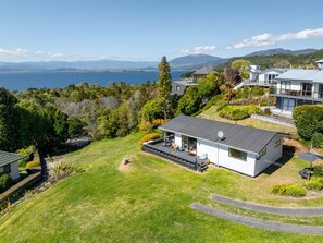 A modern house with a large deck, surrounded by lush greenery and a view of a lake and mountains. - Koromiko Rest - Omori *pet friendly* (Omori)