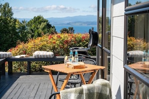 Une terrasse extérieure avec une table et des chaises, un barbecue et une vue sur la mer et les montagnes.