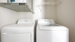 Two white front-loading washing machines in a laundry room with a metal shelf above and a white drying rack on the wall. - Landing | Stunning 1BD, Gym (Birmingham)