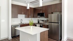 A modern kitchen with dark wooden cabinets, stainless steel appliances, and a central island. - Landing | Spectacular 1BD, Gym (Birmingham)