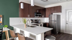 A modern kitchen with a central island, stainless steel appliances, and dark wooden cabinets. - Landing | Incredible 1BD, Gym (Birmingham)
