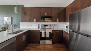 A modern kitchen with stainless steel appliances, wooden cabinets, and a white countertop. - Landing | Amazing 1BD, Gym (Birmingham)