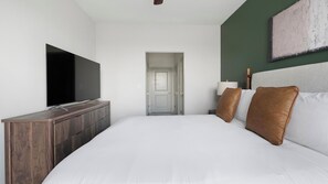 A hotel room with a large bed, a flat-screen TV, a wooden dresser, and a green accent wall. - Landing | Amazing 1BD, Gym (Birmingham)