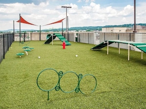 Ein Dachgarten mit Kunstgrasanlage, Spielgeräten und Blick auf die Stadtlandschaft.