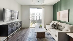 A modern living room with a flat-screen TV, a sofa, a coffee table, and a view through a sliding glass door. - Landing | Amazing 1BD, Gym (Birmingham)