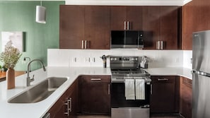 A modern kitchen with stainless steel appliances, a double sink, and wooden cabinets. - Landing | Amazing 1BD, Gym (Birmingham)