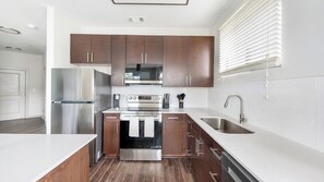 A modern kitchen with stainless steel appliances, wooden cabinets, and a white countertop. - Landing | Stunning 2BD, Gym (Birmingham)