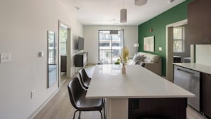 Eine moderne Küche mit einer zentralen Kochinsel, einem Essbereich mit Stühlen, einer Couch und einer Wand in Grüntönen.