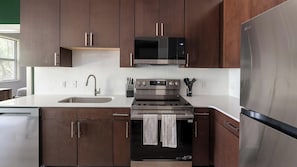 Eine moderne Küche mit Edelstahlgeräten, darunter ein Kühlschrank, eine Mikrowelle und ein Ofen, mit Holzausbau und weißen Arbeitsplatten.